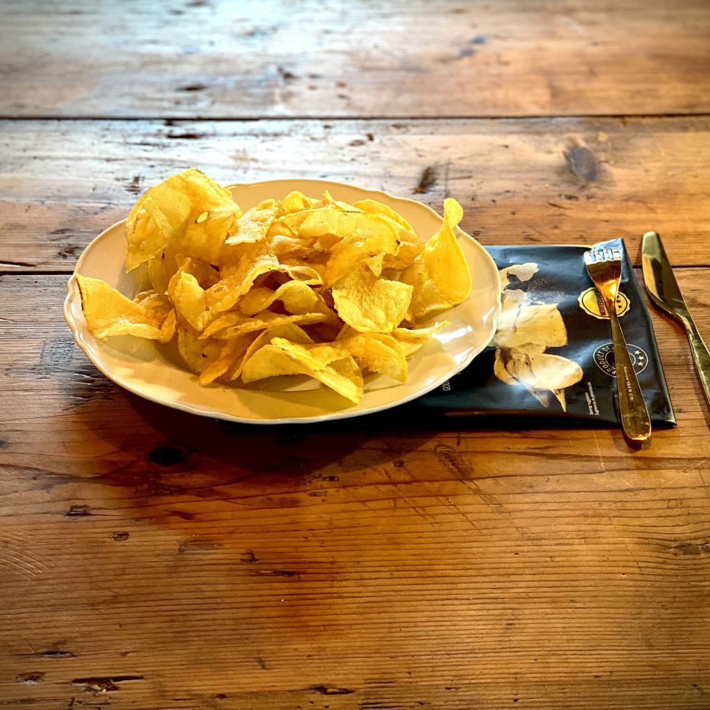 Des chips à la truffe dans une assiette blanche posée sur un plan de travail en bois